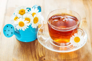 Chamomile tea in a glass cup and chamomile flowers in a small blue watering can